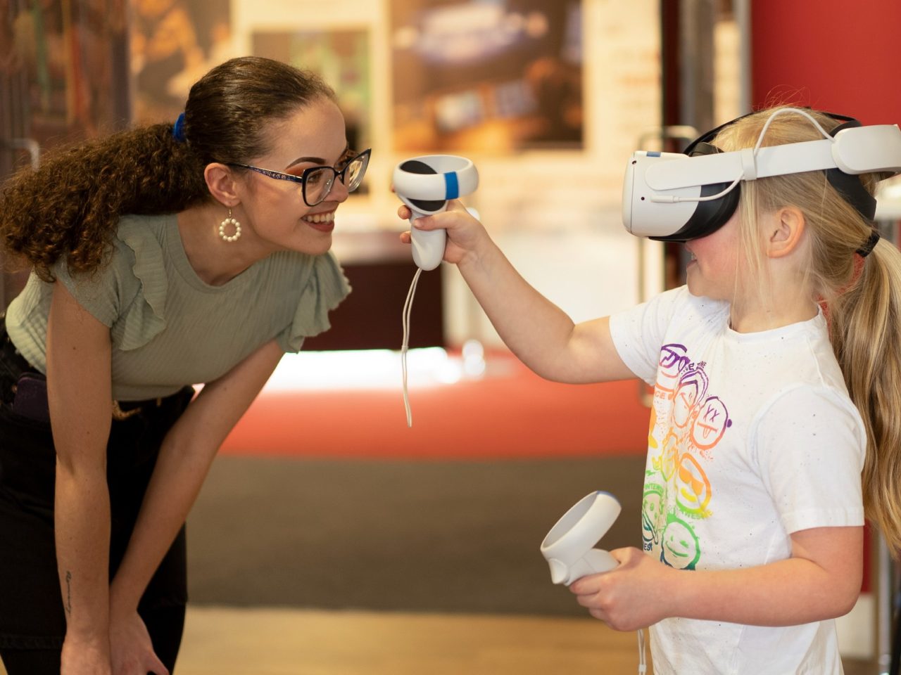 Lucy smiling with a young person who is wearing a VR headset