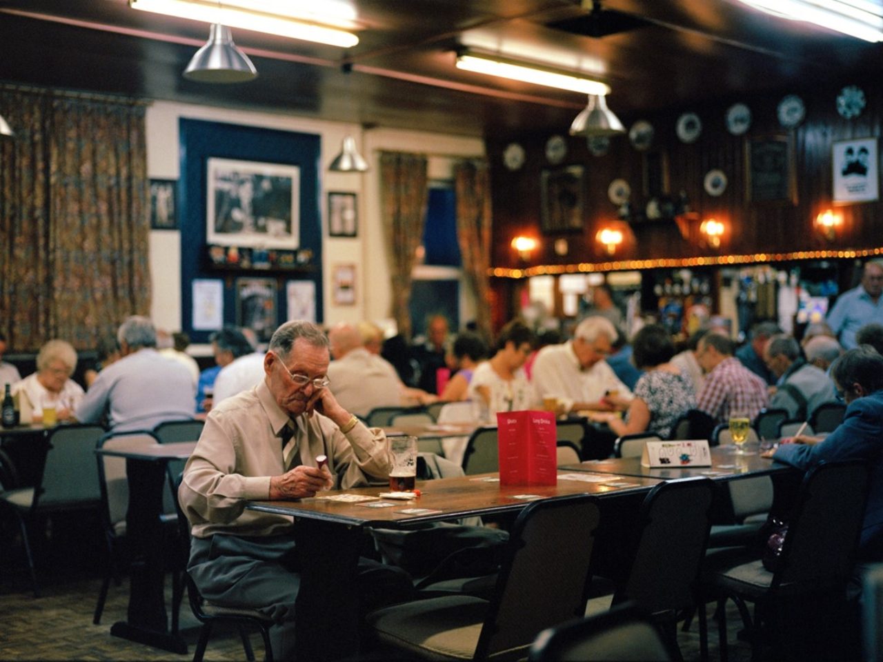 An older gentleman sits in a social hall as he plays bingo.